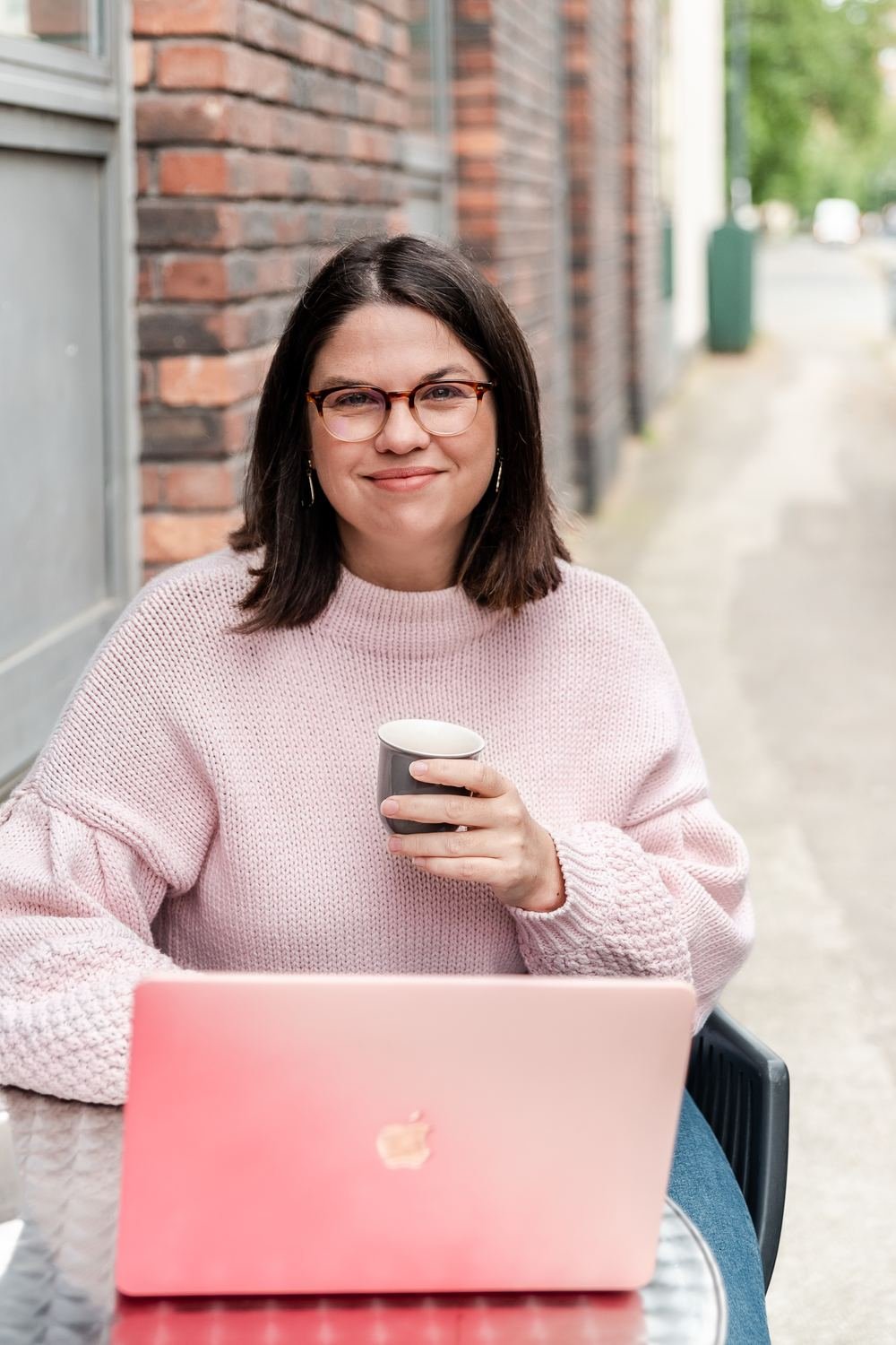 Cheryl Oliver smiling at a café table with her pink laptop and a coffee