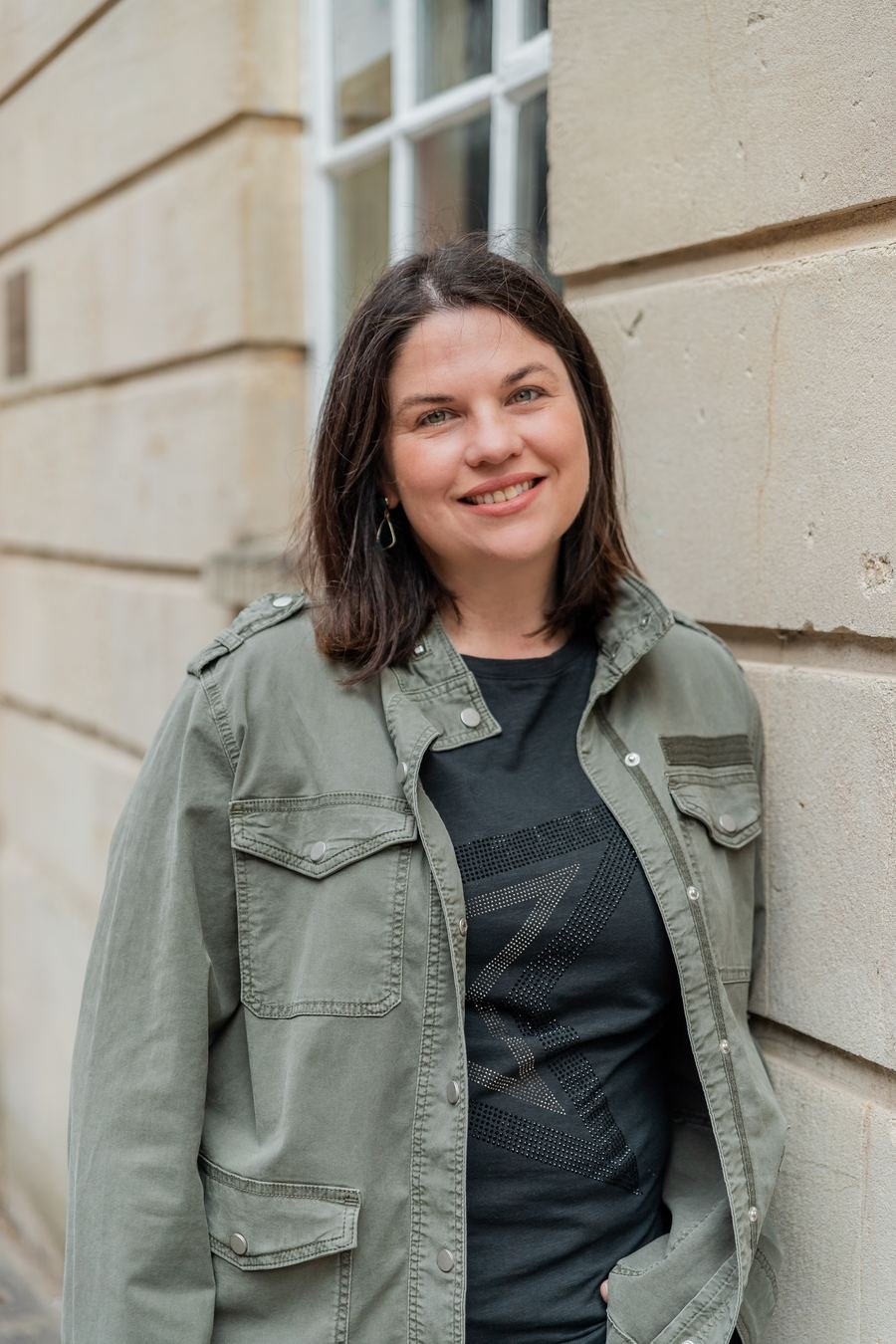Cheryl Oliver smiling, leaning against a sandstone wall